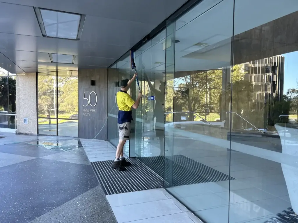 Coates Window Cleaning technician washing the glass entrance of an office building in Perth