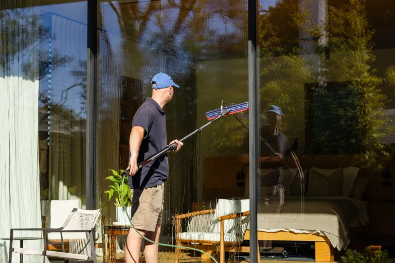 Cleaning tall glass doors with a long-handled squeegee on a sunny Perth day