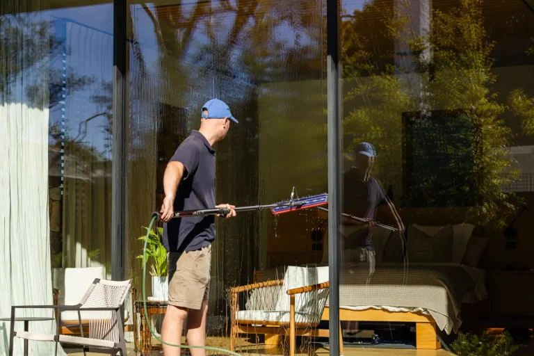 Washing the glass doors of a modern Perth home, furniture visible through the pane