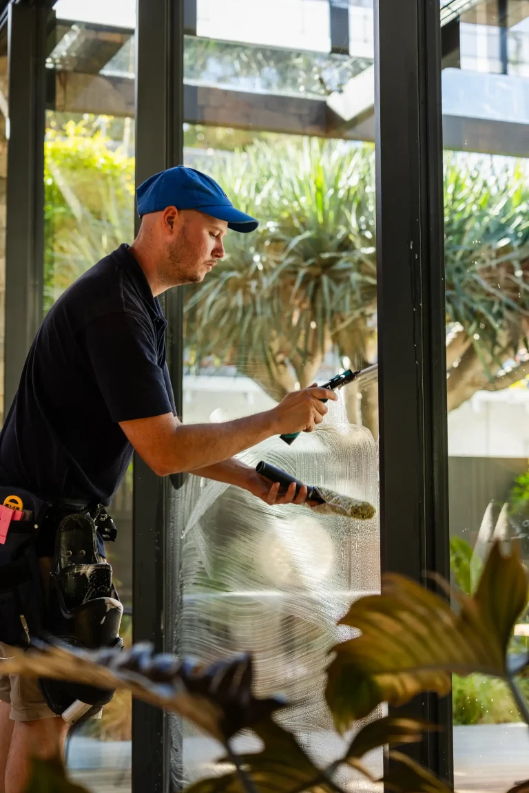 Technician cleaning floor-to-ceiling windows inside a bright Perth home