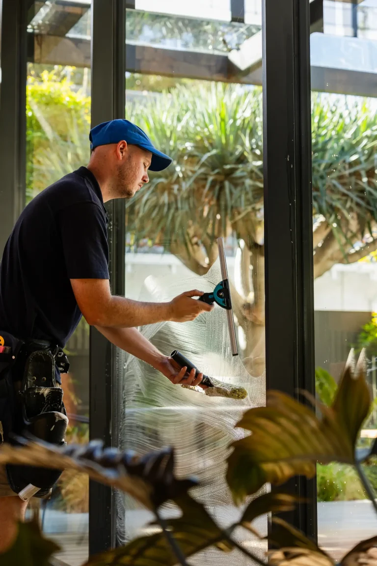 Detailing a large glass window with a squeegee at a Perth home, greenery beyond