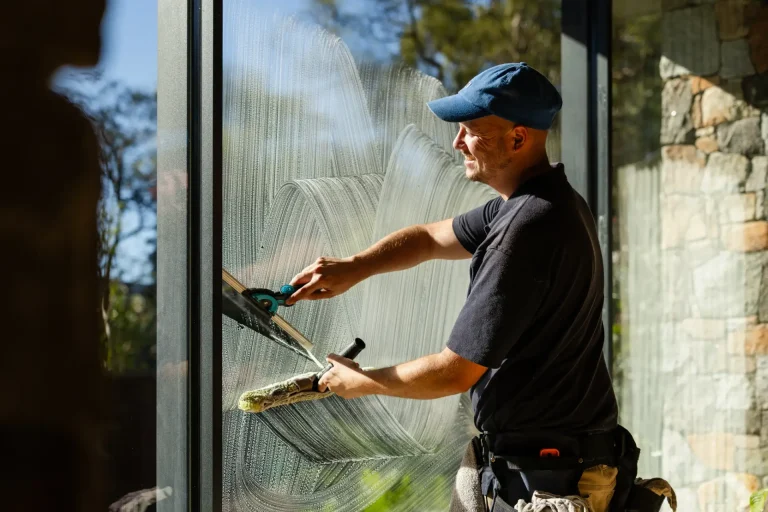 Coates Window Cleaning technician with tool belt squeegeeing a large glass window
