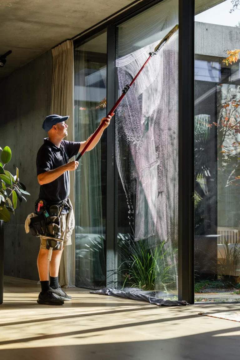 Cleaning tall interior glass panels with a long-handled tool in Perth