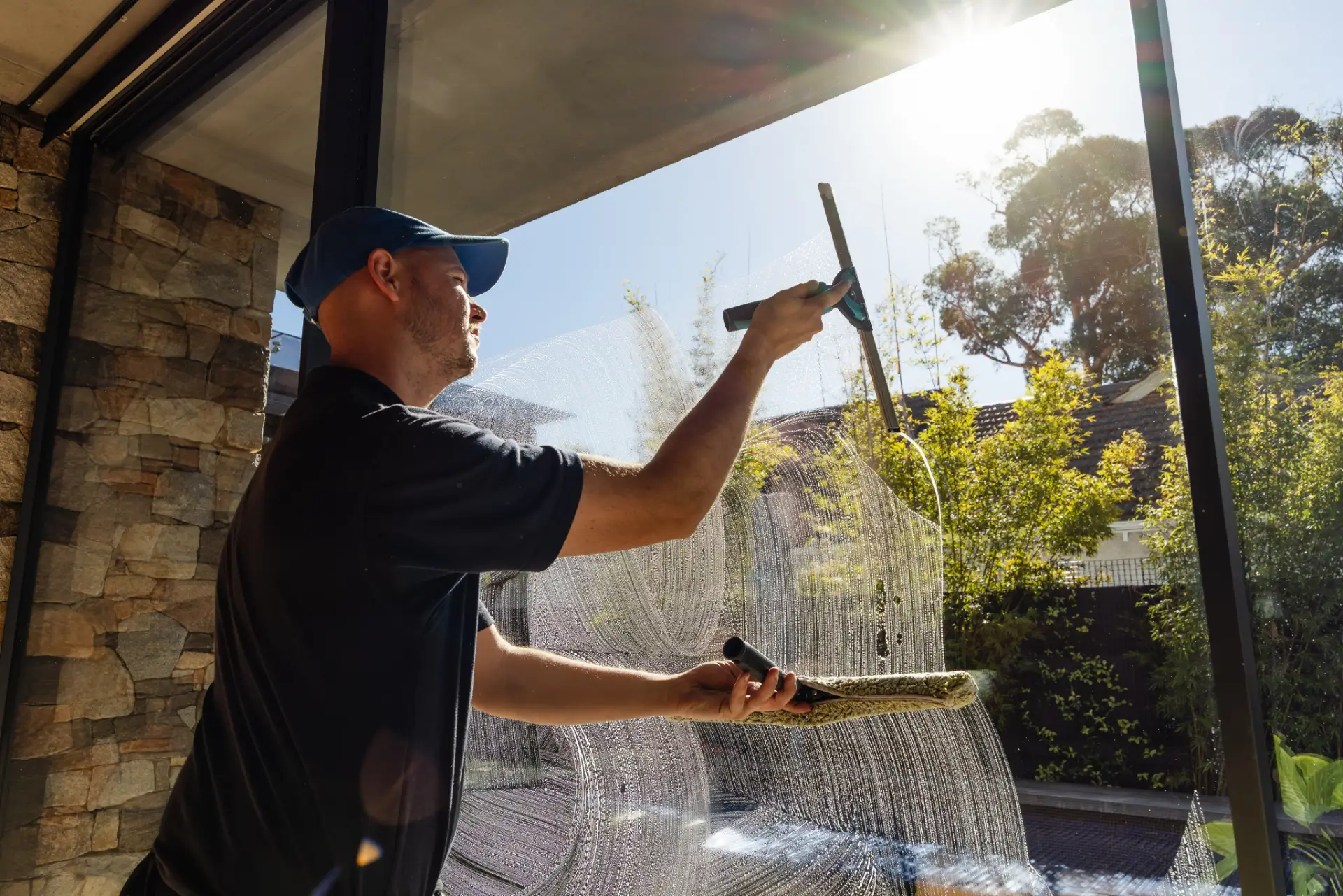 Window cleaner squeegeeing a large sunlit pane at a Perth property