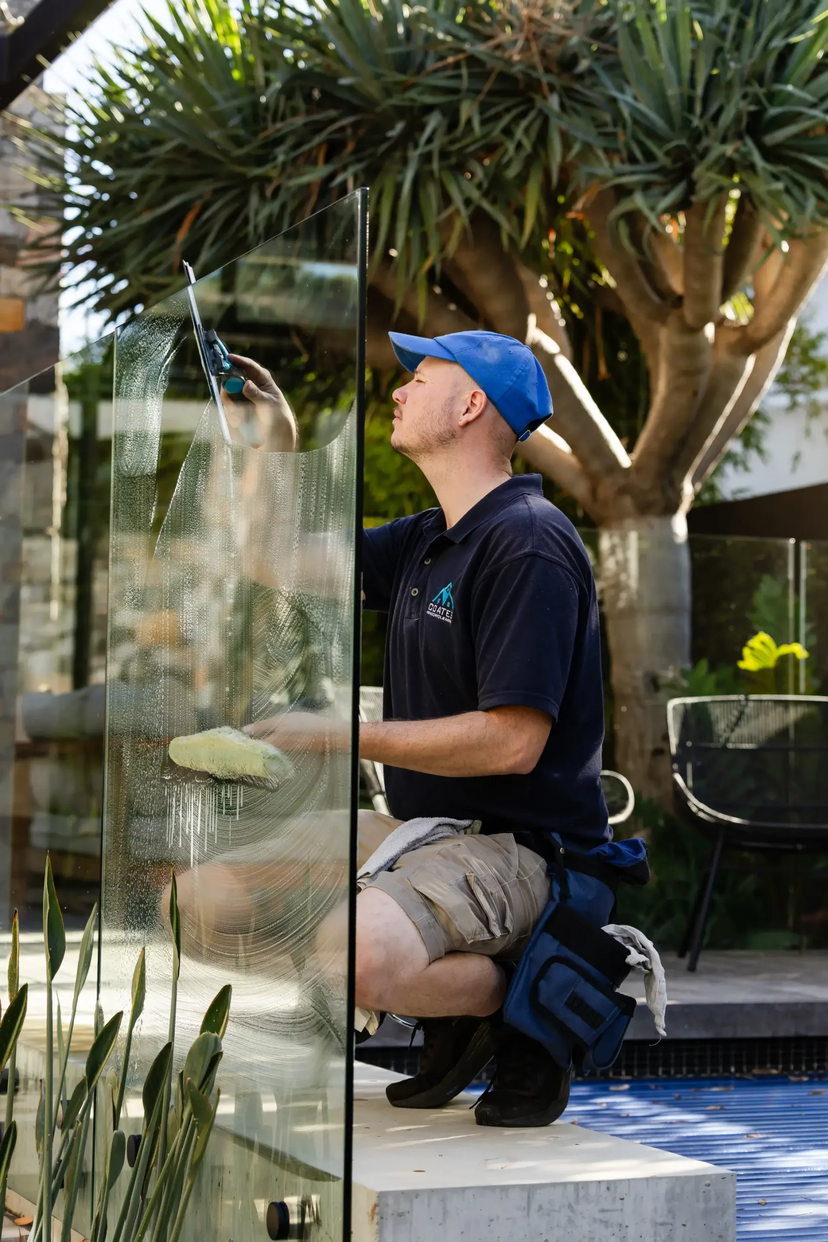 Cleaning a glass pool fence with squeegee and sponge in a Perth backyard