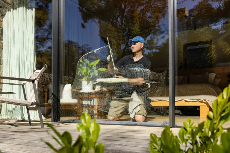 Washing a sliding glass door from outside at a Perth home, furniture visible inside