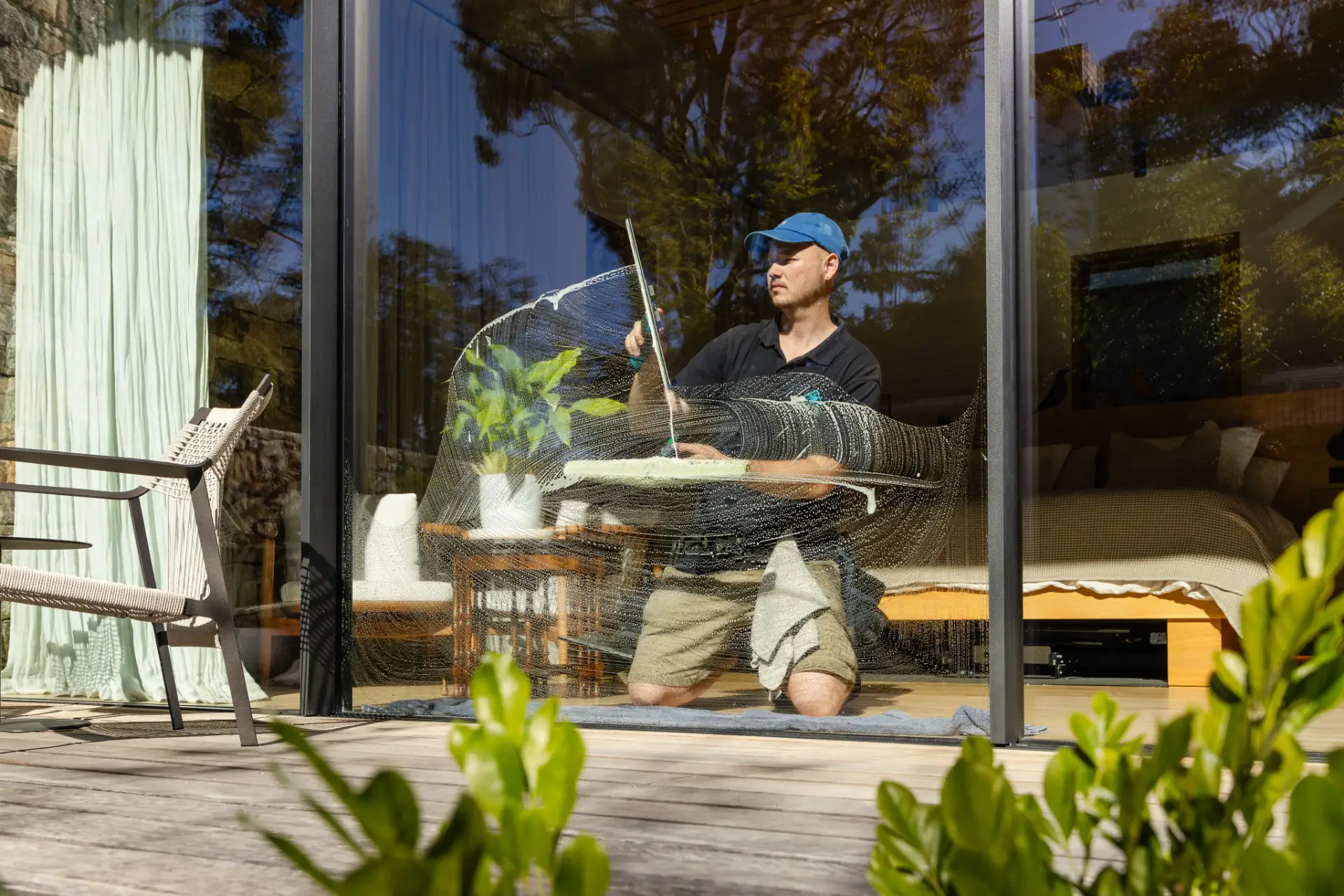 Washing a sliding glass door from outside at a Perth home, furniture visible inside