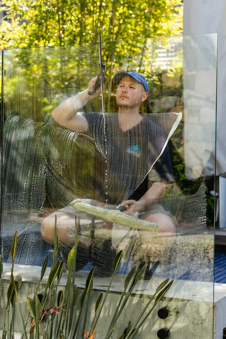 Squeegee and sponge work on an outdoor window surrounded by greenery in Perth