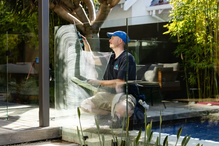 Cleaning pool-fence glass with squeegee and sponge on a sunny Perth day