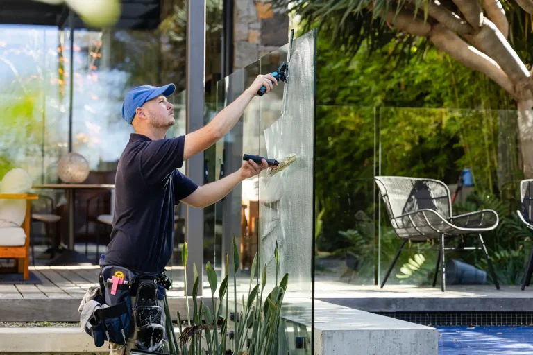 Cleaning outdoor glass near a pool area with lush plants at a Perth home